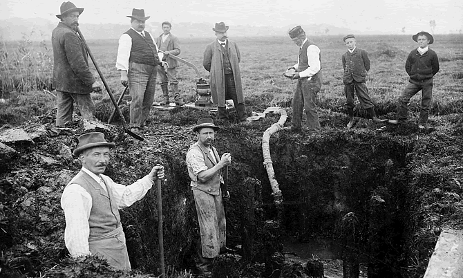 Auf diesem Bild zu sehen ist Jakob Messikommer (dritter von rechts), wie er dem Präsidenten der Antiquarischen Gesellschaft Pfäffikon einen geborgenen Mühlstein übergibt. Das Foto entstand im Jahr 1908. Quelle: Kantonsarchäologie Kanton Zürich